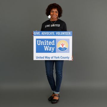 Woman smiling towards a camera holding a "United Way" sign