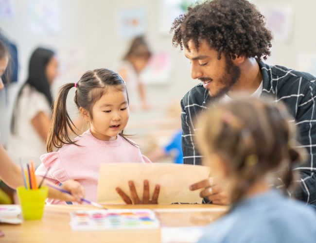 A man in a flannel shirt working with a child in a pink shirt.