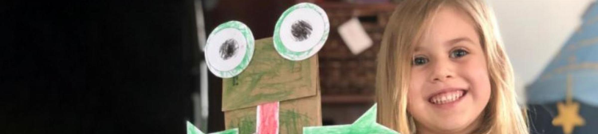 young girl holding frog paper bag puppet