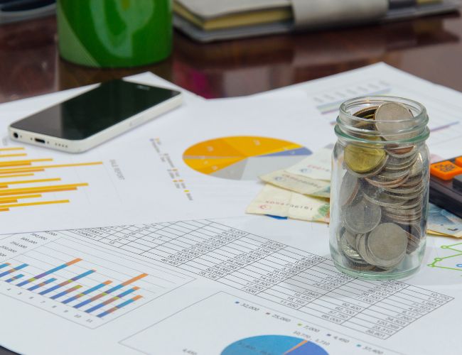 Financial charts and tables with a jar of coins on top