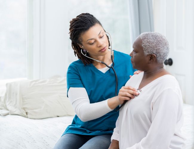 A person with a stethoscope listening to the heartbeat of an older woman
